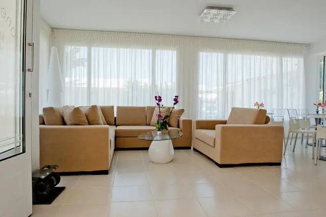 The lounge: beige sofas and tall windows with white curtains